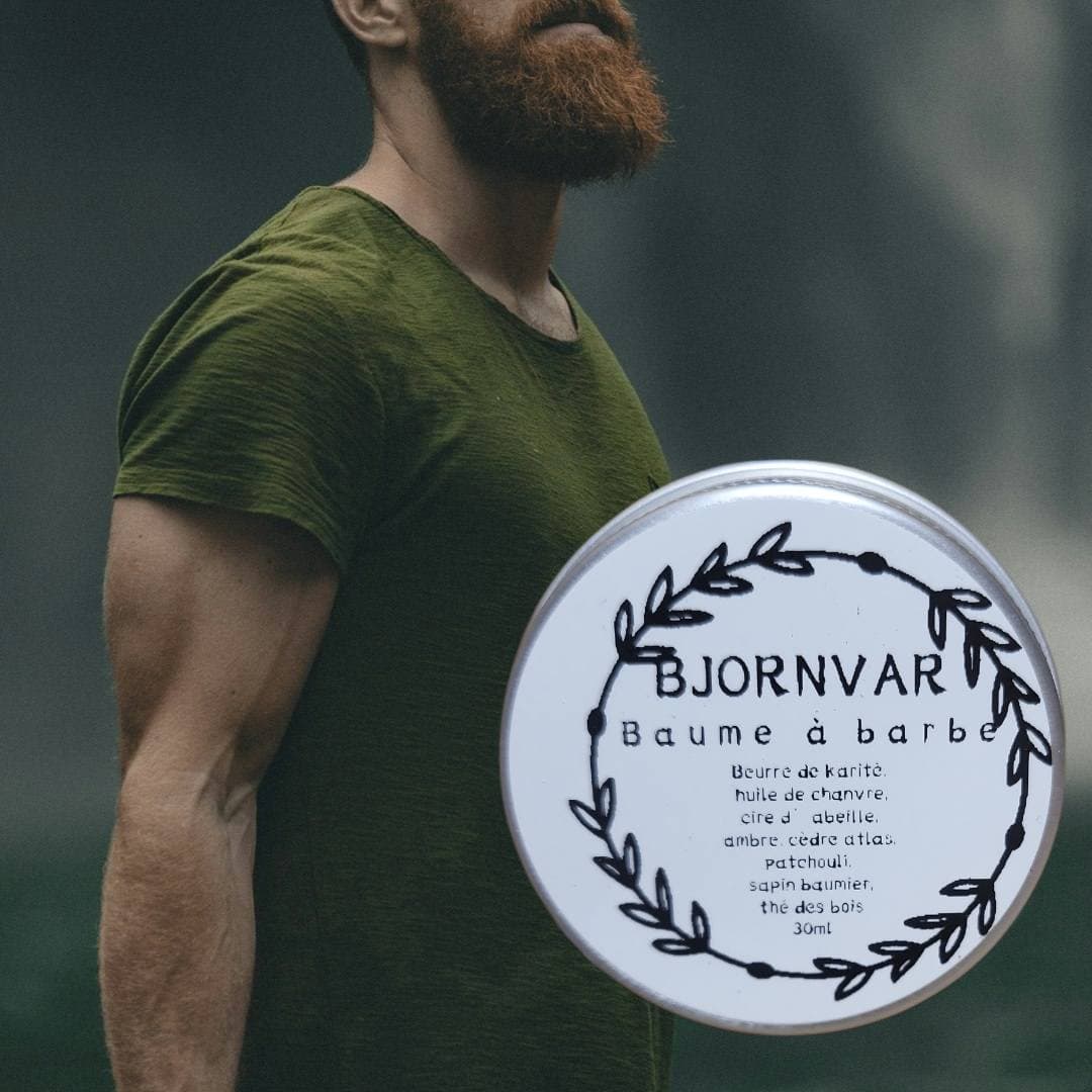 Bearded man in a green shirt with a circular tin of Bjornvar beard balm.